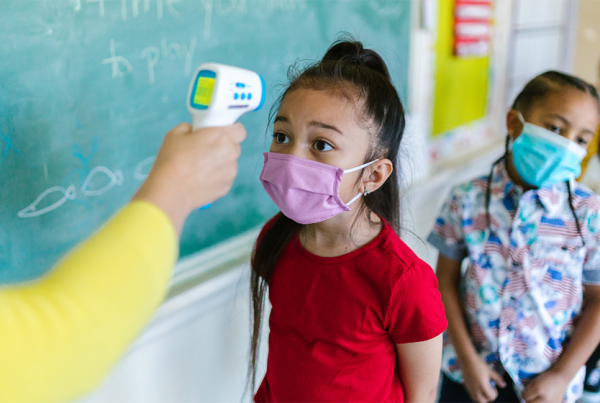 Young girl stands first in line in an elementary school classroom to get her temperature checked